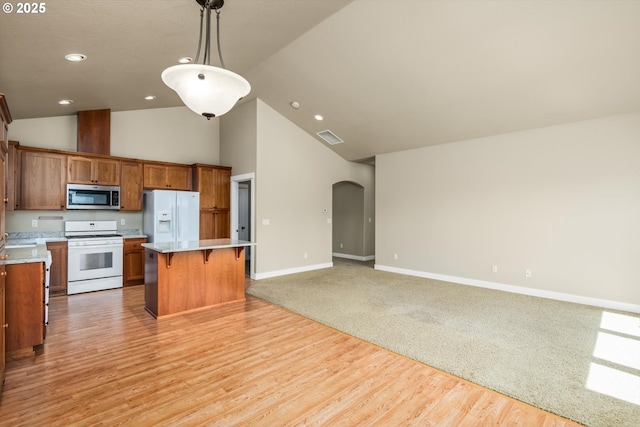 kitchen featuring a kitchen bar, arched walkways, light countertops, open floor plan, and white appliances