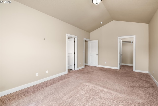 unfurnished bedroom with baseboards, lofted ceiling, a walk in closet, and carpet