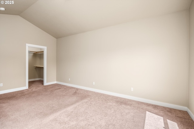 unfurnished bedroom featuring a closet, light carpet, baseboards, a walk in closet, and vaulted ceiling