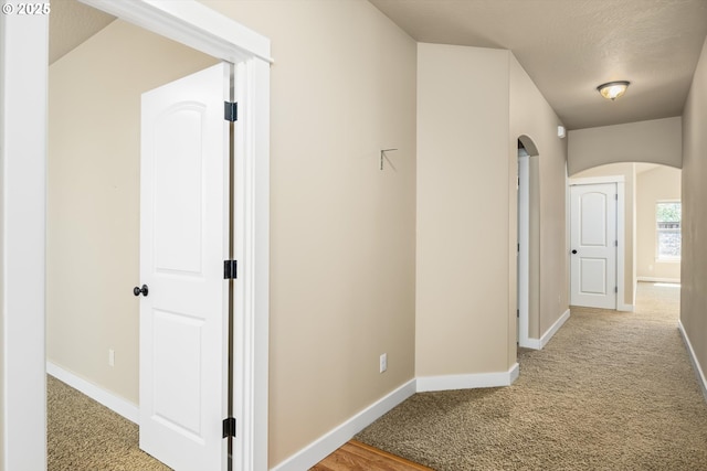hall featuring baseboards, arched walkways, and light carpet