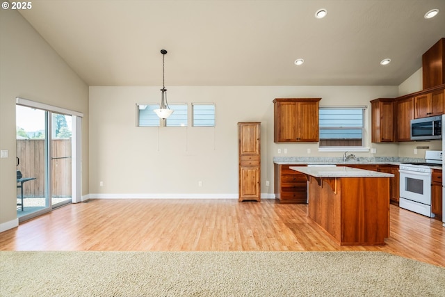 kitchen with brown cabinetry, vaulted ceiling, stainless steel microwave, white range with gas cooktop, and light wood-style floors