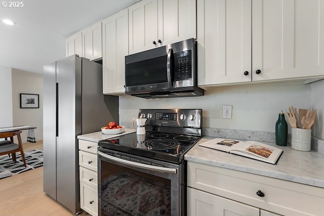 4038 NE Multnomah St, Portland, OR 97232 - kitchen with stainless steel appliances, white cabinets, light wood-style flooring, and light stone counters