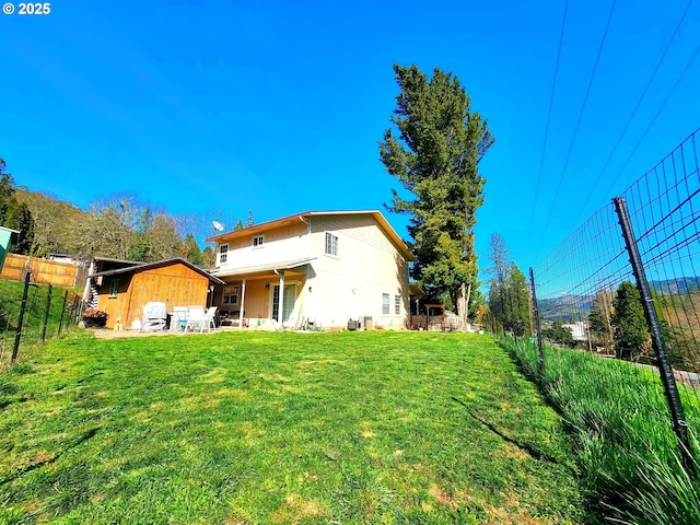 back of house with a yard, an outbuilding, a storage shed, and fence