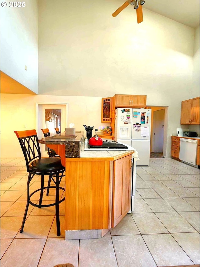 kitchen featuring a kitchen breakfast bar, white appliances, a high ceiling, light tile patterned floors, and ceiling fan