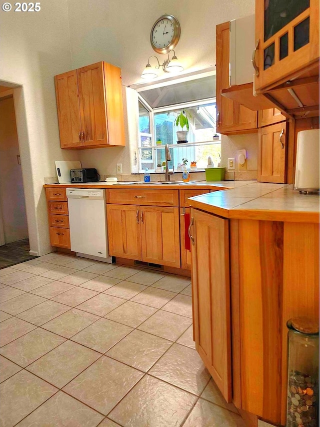 kitchen with light tile patterned floors, brown cabinetry, a peninsula, a sink, and dishwasher