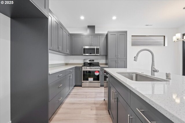 kitchen with stainless steel electric stove, a sink, light wood finished floors, light countertops, and an island with sink