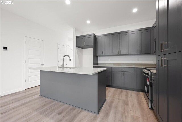 kitchen with stainless steel electric stove, a sink, light wood finished floors, light countertops, and an island with sink