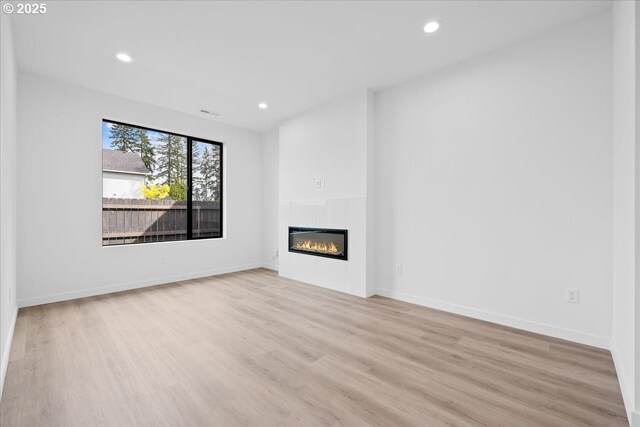 unfurnished living room featuring light wood-type flooring, recessed lighting, a glass covered fireplace, and baseboards