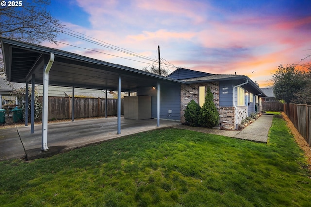 back of property at dusk with a yard, an attached carport, brick siding, and fence