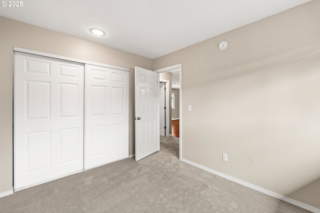 unfurnished bedroom with a closet, light carpet, and baseboards