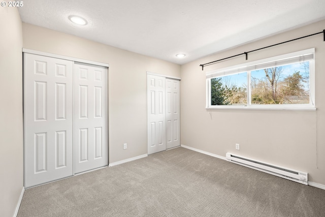 unfurnished bedroom with carpet floors, baseboards, two closets, and a baseboard radiator