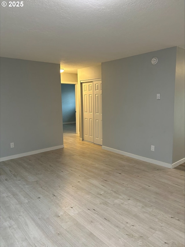 spare room featuring light wood finished floors, a textured ceiling, and baseboards