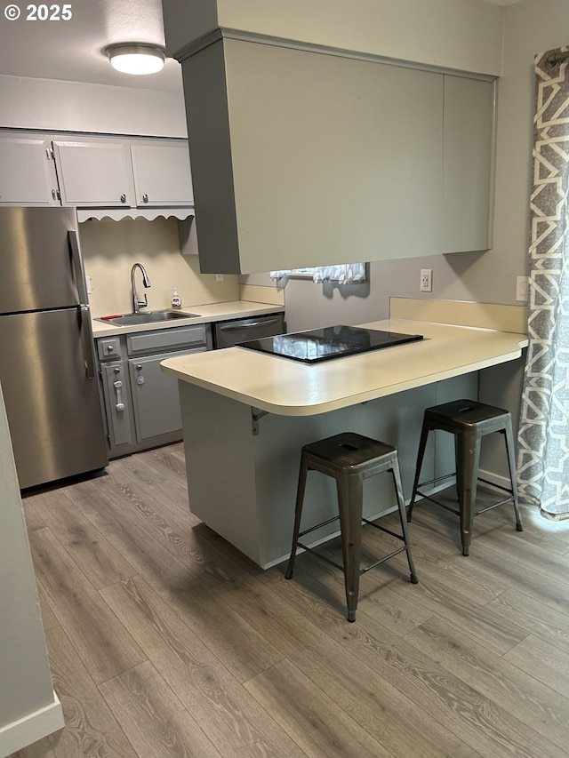 kitchen featuring light wood finished floors, dishwasher, light countertops, freestanding refrigerator, and a sink