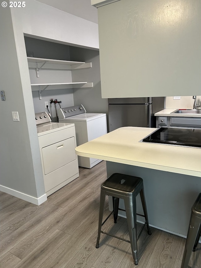 laundry area with baseboards, laundry area, light wood-style flooring, a sink, and washing machine and dryer