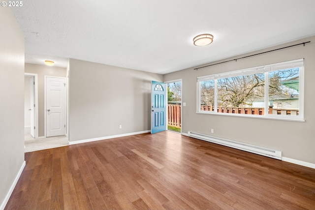 empty room featuring baseboard heating, baseboards, and wood finished floors