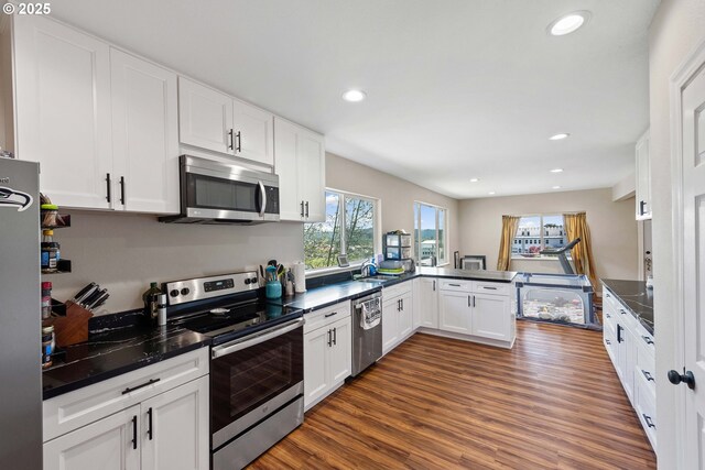 kitchen featuring appliances with stainless steel finishes, dark countertops, a sink, white cabinetry, and recessed lighting