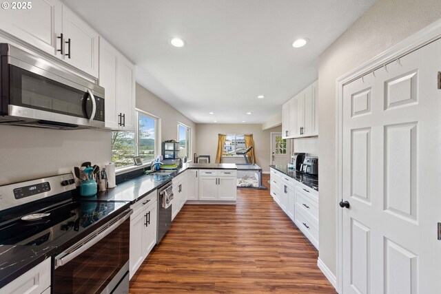 kitchen with appliances with stainless steel finishes, dark wood-type flooring, a peninsula, dark countertops, and recessed lighting
