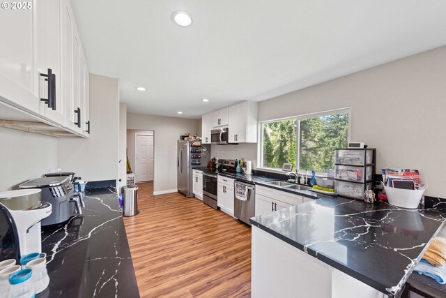 kitchen with stainless steel appliances, a sink, light wood-style flooring, dark countertops, and white cabinetry