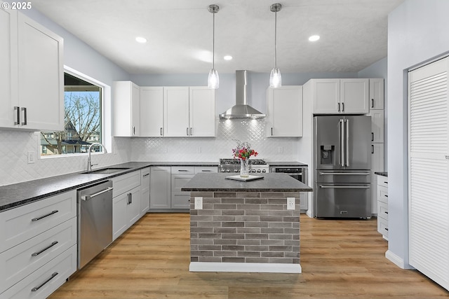 kitchen featuring dark countertops, wall chimney range hood, stainless steel appliances, and a sink