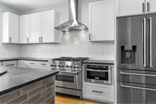 kitchen featuring stainless steel appliances, white cabinets, backsplash, and wall chimney exhaust hood