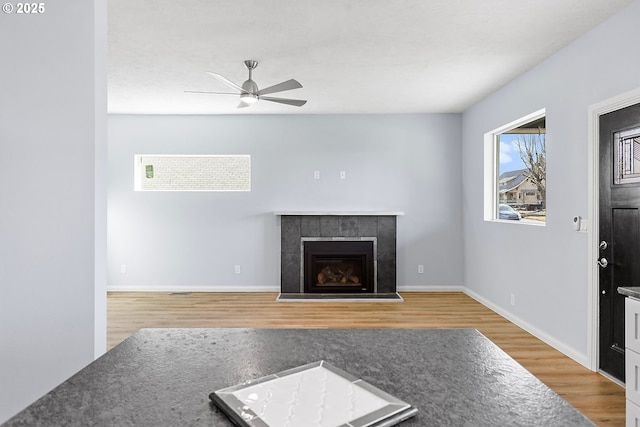 unfurnished living room featuring ceiling fan, a tiled fireplace, wood finished floors, and baseboards