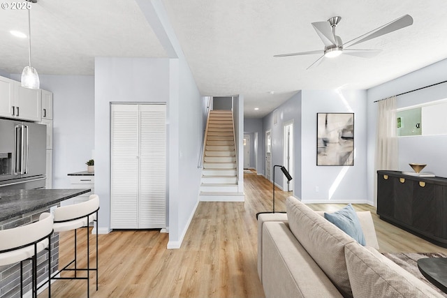 living area with stairs, light wood-type flooring, a ceiling fan, and baseboards