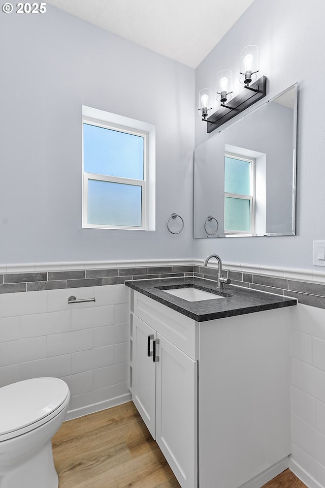 bathroom featuring toilet, a wainscoted wall, wood finished floors, vanity, and tile walls