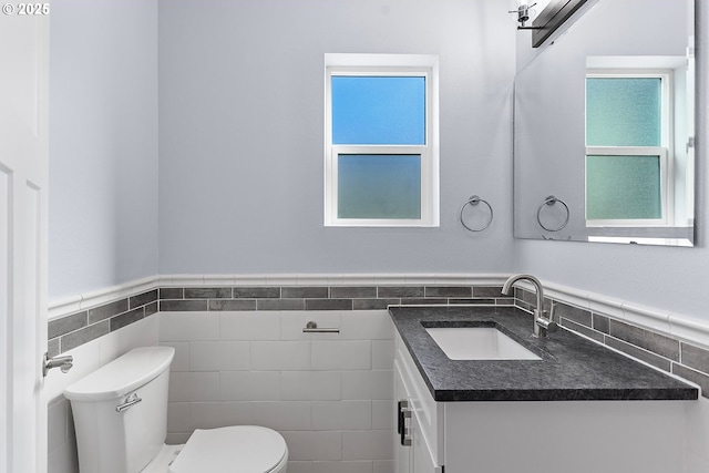 bathroom with toilet, wainscoting, tile walls, and vanity