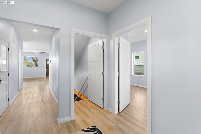 hallway with light wood-type flooring, baseboards, and an upstairs landing