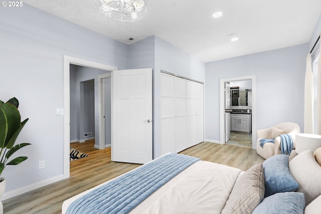 bedroom with light wood finished floors, a closet, visible vents, ensuite bathroom, and baseboards