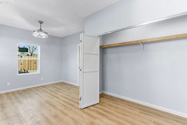 unfurnished bedroom featuring light wood-style flooring, a closet, baseboards, and a notable chandelier