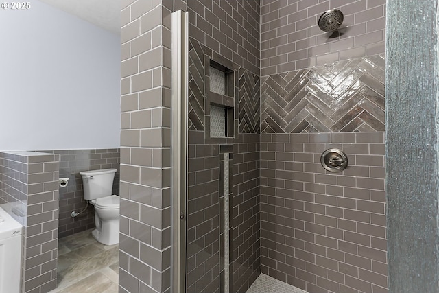 bathroom with a wainscoted wall, tiled shower, toilet, and tile walls