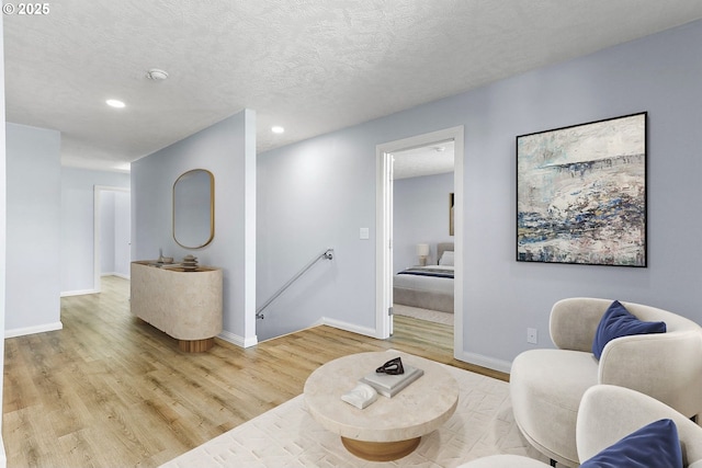 living room featuring a textured ceiling, light wood finished floors, recessed lighting, and baseboards