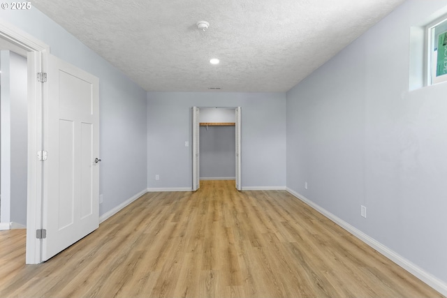 empty room featuring a textured ceiling, light wood-type flooring, and baseboards