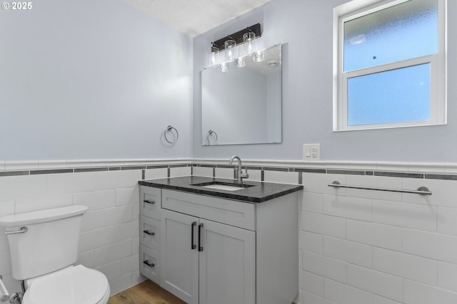 bathroom with toilet, a wainscoted wall, tile walls, and vanity