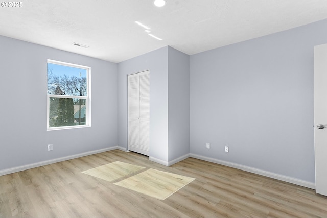 unfurnished bedroom with a closet, wood finished floors, visible vents, and baseboards