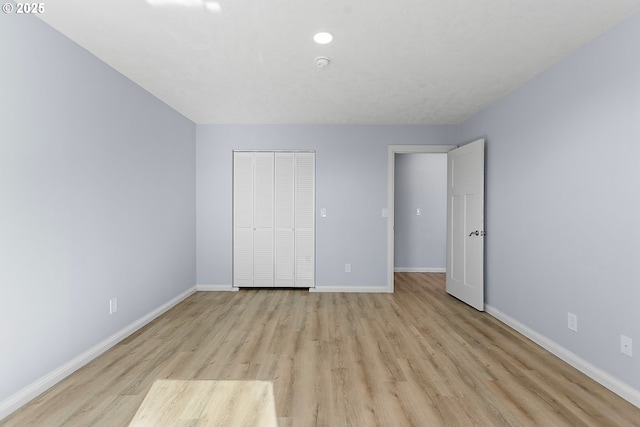 unfurnished bedroom featuring light wood-style flooring, baseboards, and a closet