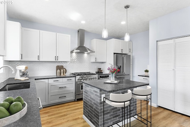 kitchen with wall chimney range hood, premium appliances, a sink, and light wood-style flooring