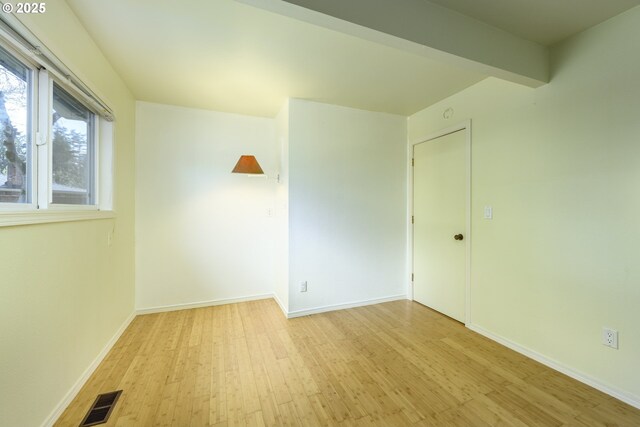 spare room with baseboards, visible vents, wood finished floors, and beamed ceiling