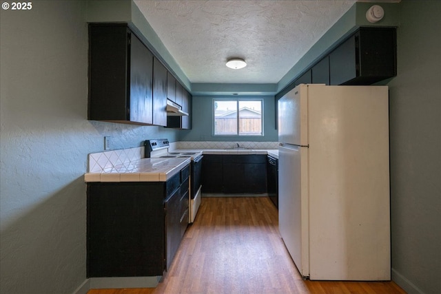 kitchen with tile counters, white appliances, a textured ceiling, and light hardwood / wood-style flooring