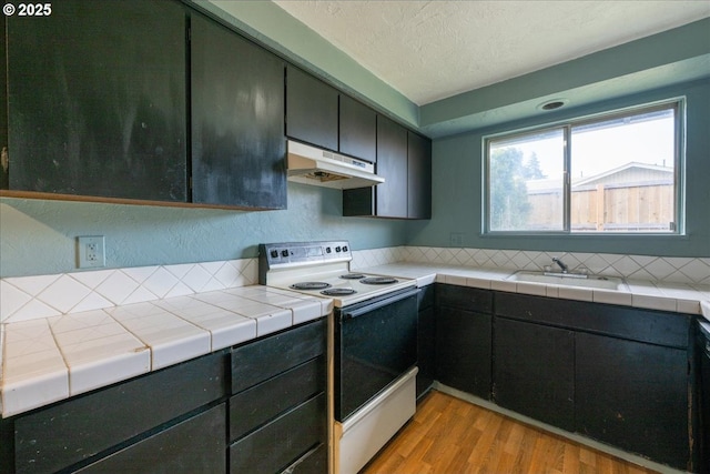 kitchen with sink, white electric range oven, light hardwood / wood-style flooring, tile countertops, and a textured ceiling