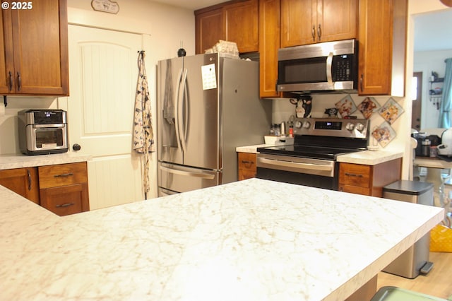 kitchen featuring appliances with stainless steel finishes, light stone countertops, and brown cabinets