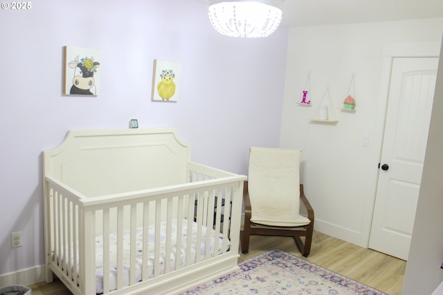 bedroom with an inviting chandelier, a nursery area, baseboards, and wood finished floors