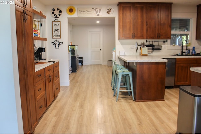 kitchen featuring light wood-style flooring, a sink, a kitchen breakfast bar, light countertops, and stainless steel dishwasher