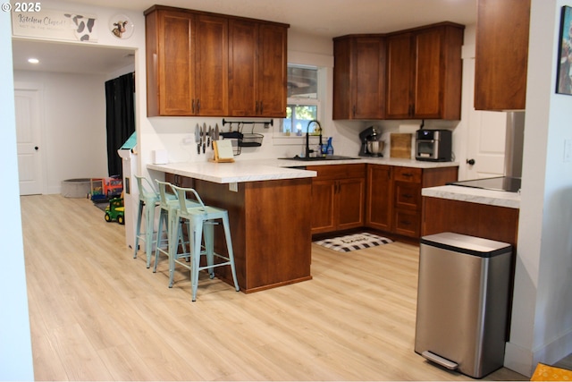 kitchen with light wood-style flooring, a breakfast bar, a sink, and a peninsula