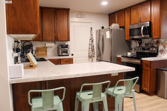 kitchen with stainless steel appliances, light countertops, light wood-style flooring, and a peninsula