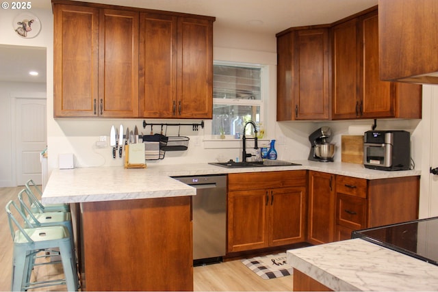 kitchen with a peninsula, a sink, light countertops, stainless steel dishwasher, and light wood finished floors