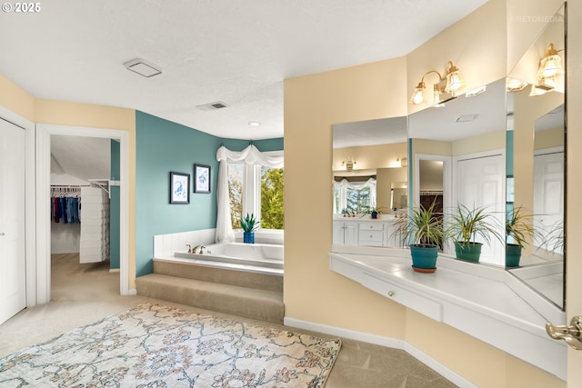 bathroom featuring vanity, baseboards, a spacious closet, visible vents, and a garden tub