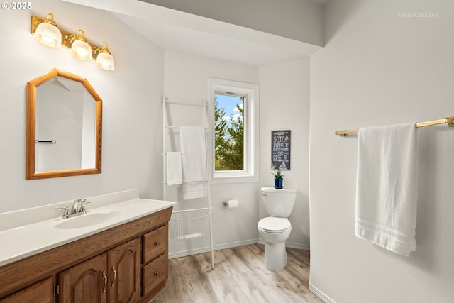 bathroom with toilet, vanity, wood finished floors, and baseboards