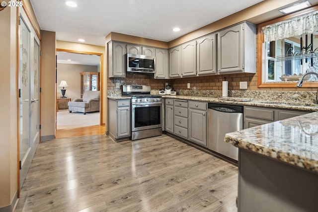 kitchen featuring stainless steel appliances, gray cabinetry, and light stone counters